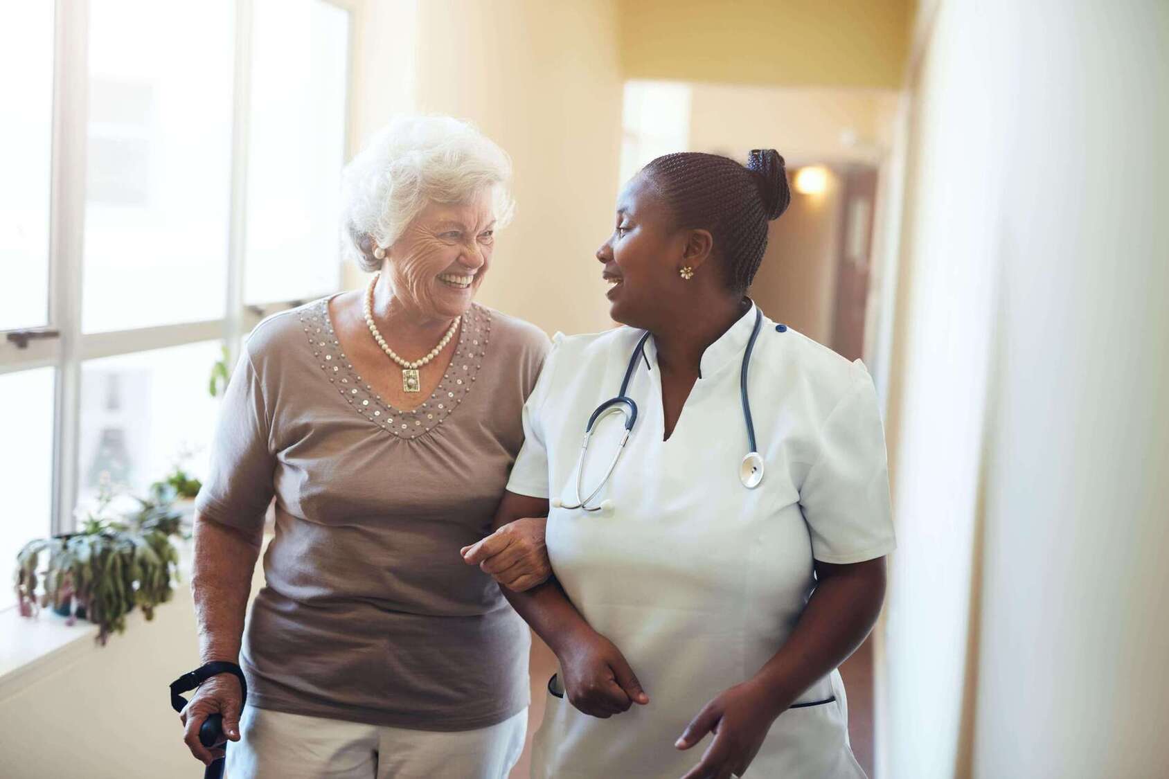 Elderly Care Nurse helping a woman to walk through the corridors